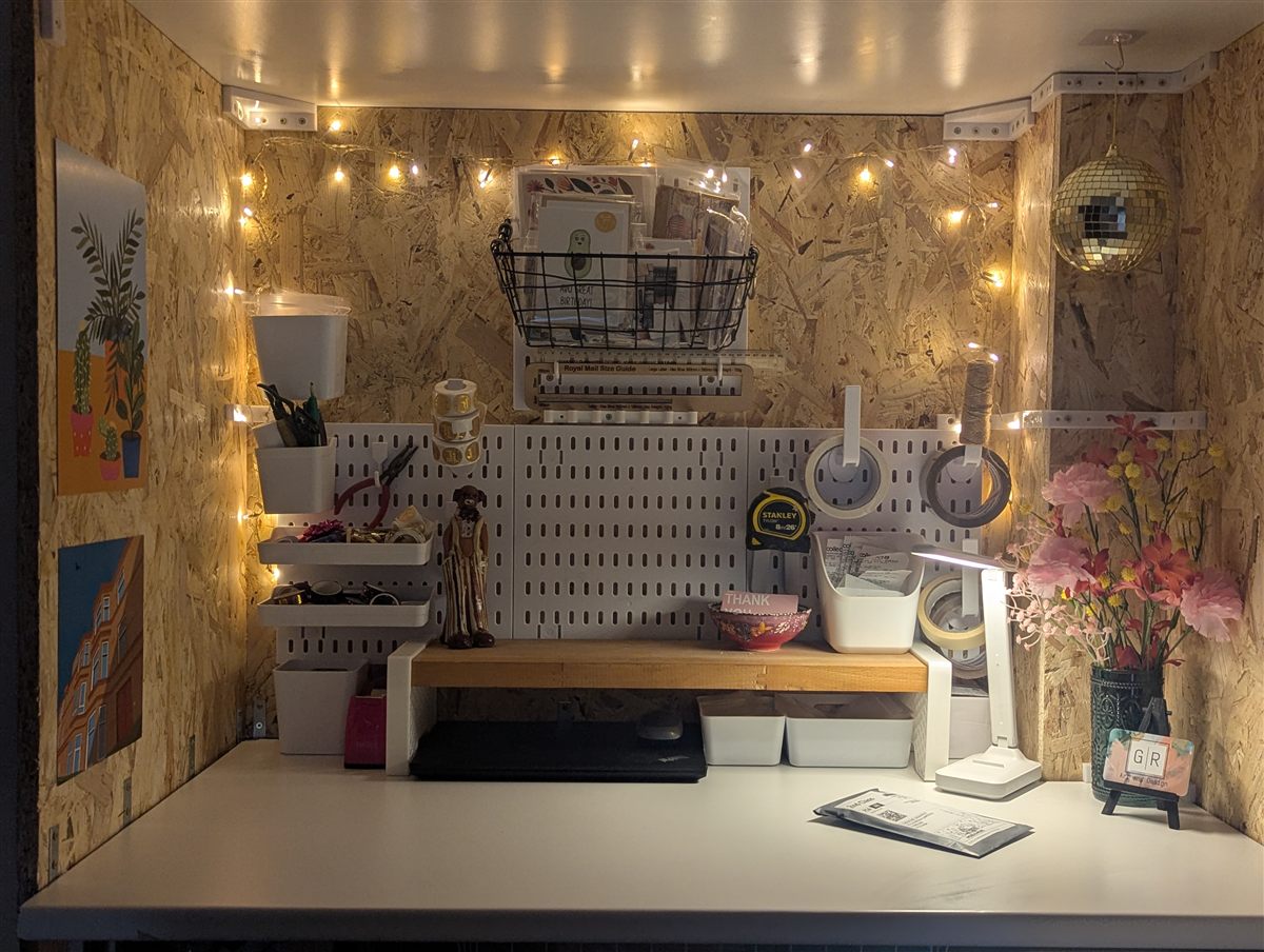 The Moss & Muse packing station — a cosy desk nook with pegboard storage, fairy lights, washi tape rolls and a Royal Mail size guide